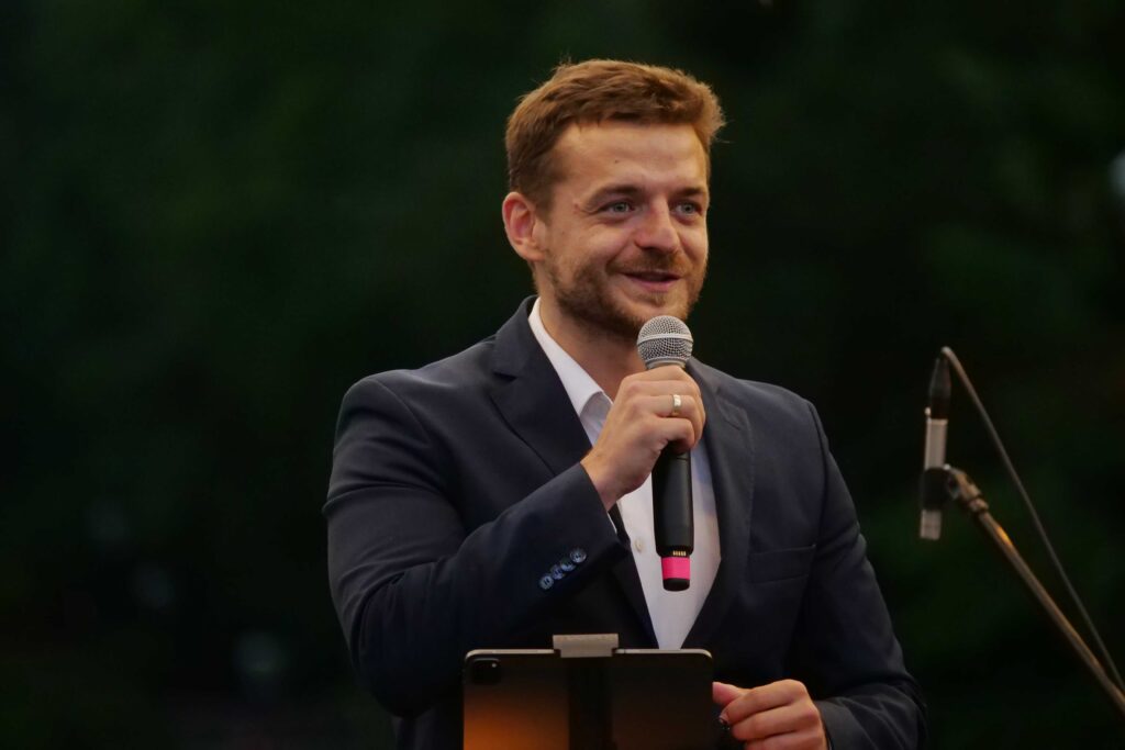 Burmistrz miasta Wojkowice Tomasz Szczerba na scenie podczas wieczorku muzycznego z Five O'Clock Orchestra w Parku Miejskim w Wojkowicach 2 lipca 2022