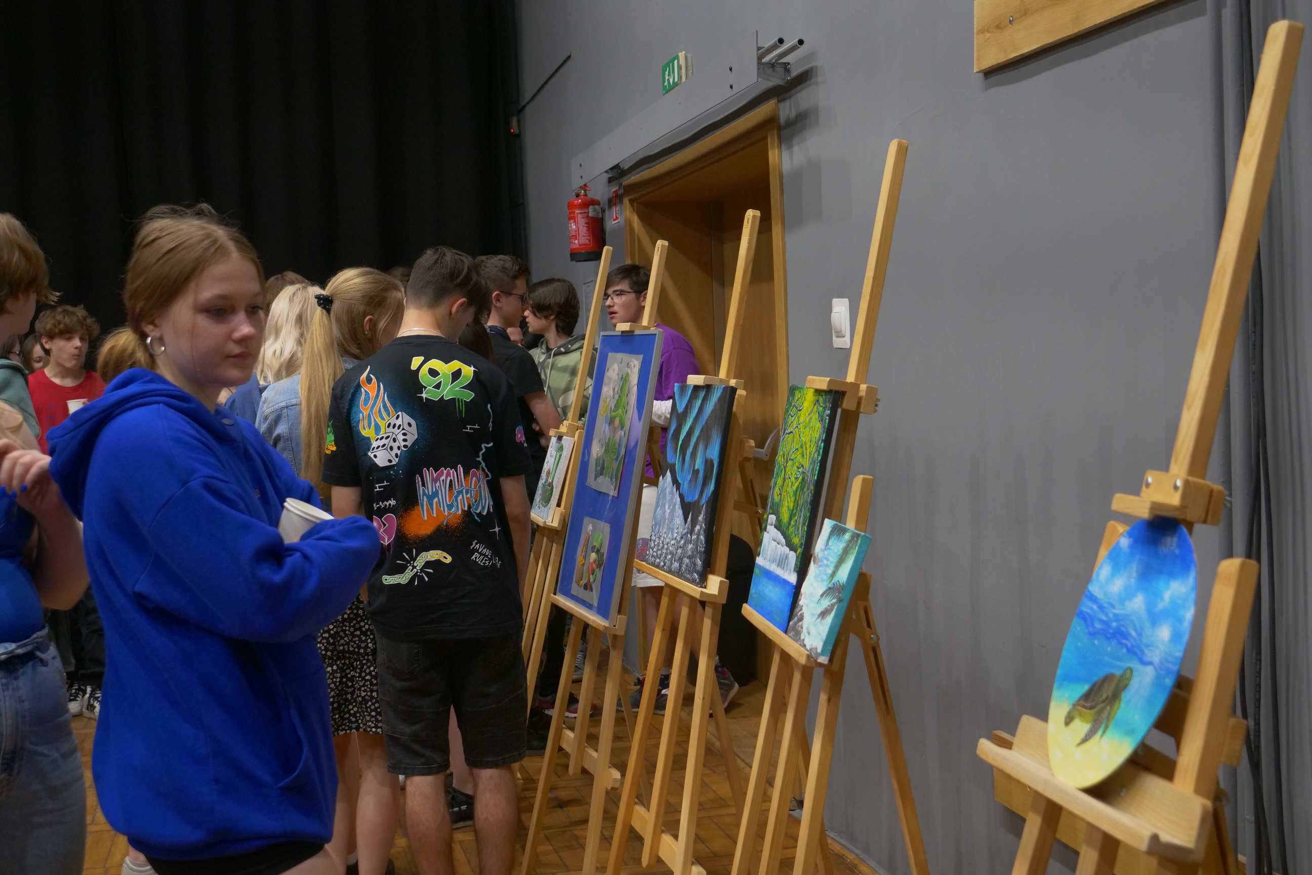 uczniowie oglądający obrazy na wernisażu malarskiego "Podróże wyobraźni" uczniów ZSOiT w Wojkowicach w Miejskim Ośrodku Kultury w Wojkowicach